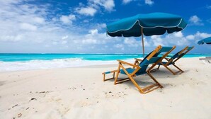 A beach with two blue lounge chairs and a matching umbrella. - Destin Beachfront Oasis (Miramar Beach)