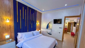 Quarto moderno com cama grande, mesas de cabeceira, televisão e espelho.