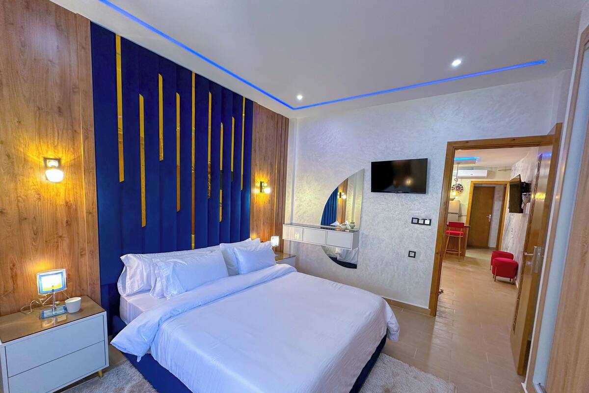 A modern bedroom with a large bed, bedside tables, a TV, and a mirror.