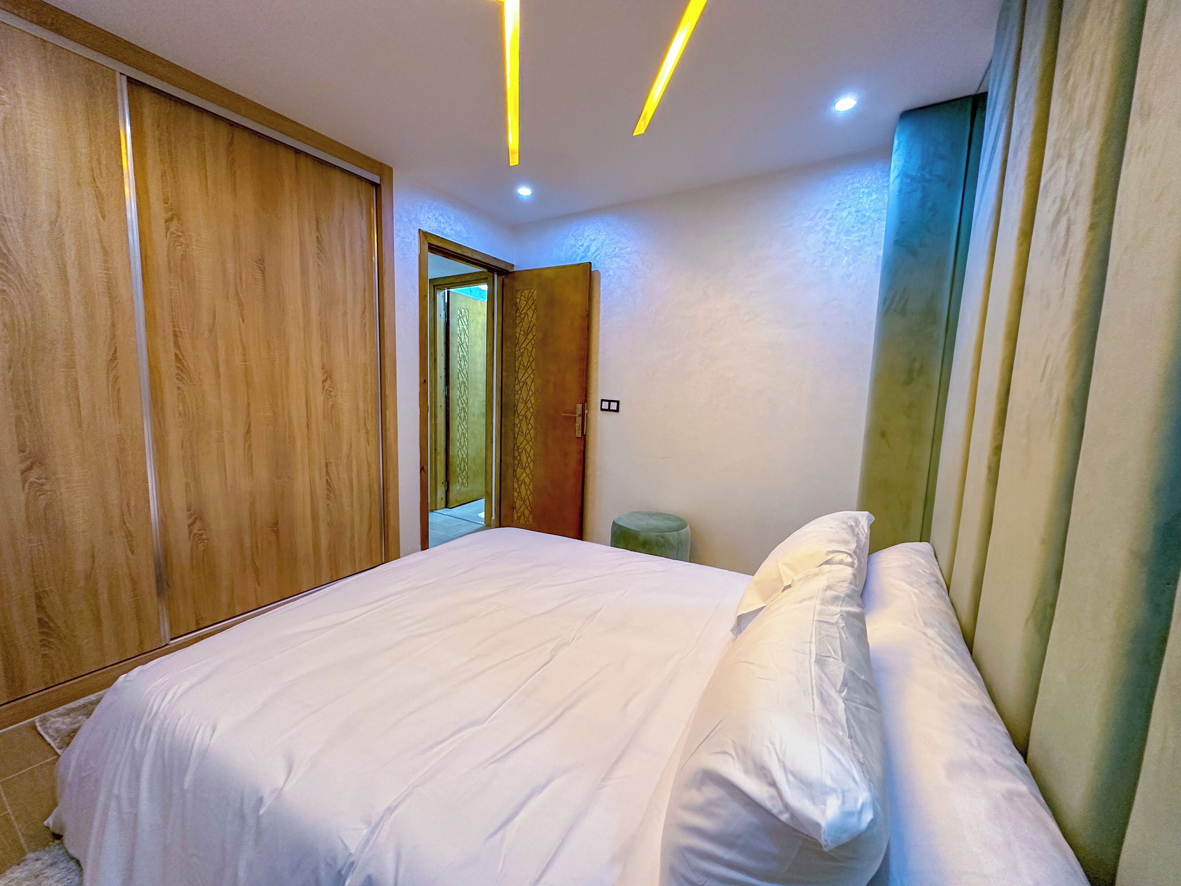 Une chambre à coucher avec un lit, une armoire en bois et un tabouret vert.