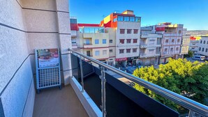 Varanda com grade de metal dando para uma rua com edifícios e árvores.