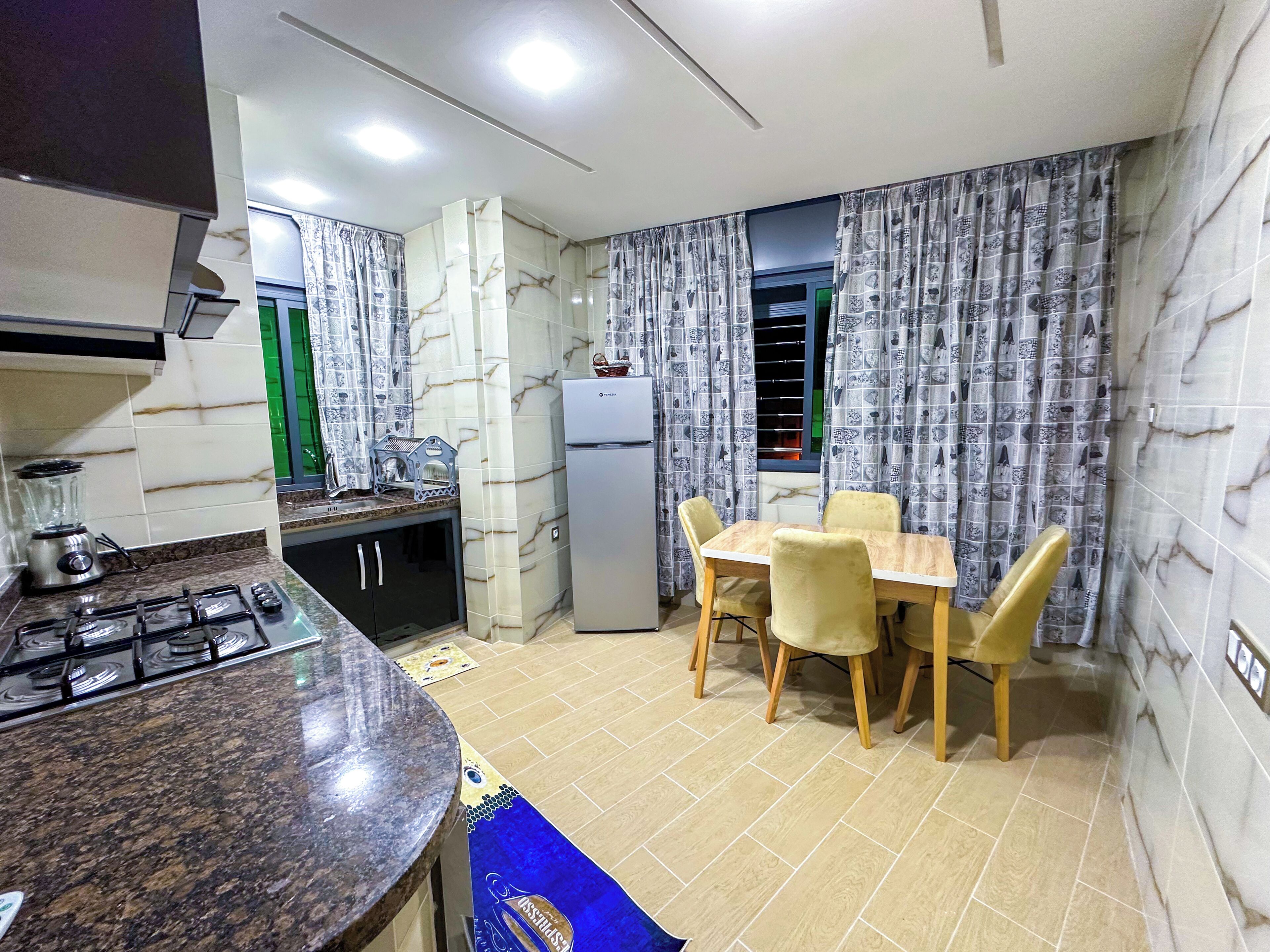 A compact kitchen with a gas stove, a refrigerator, and a dining table with chairs.