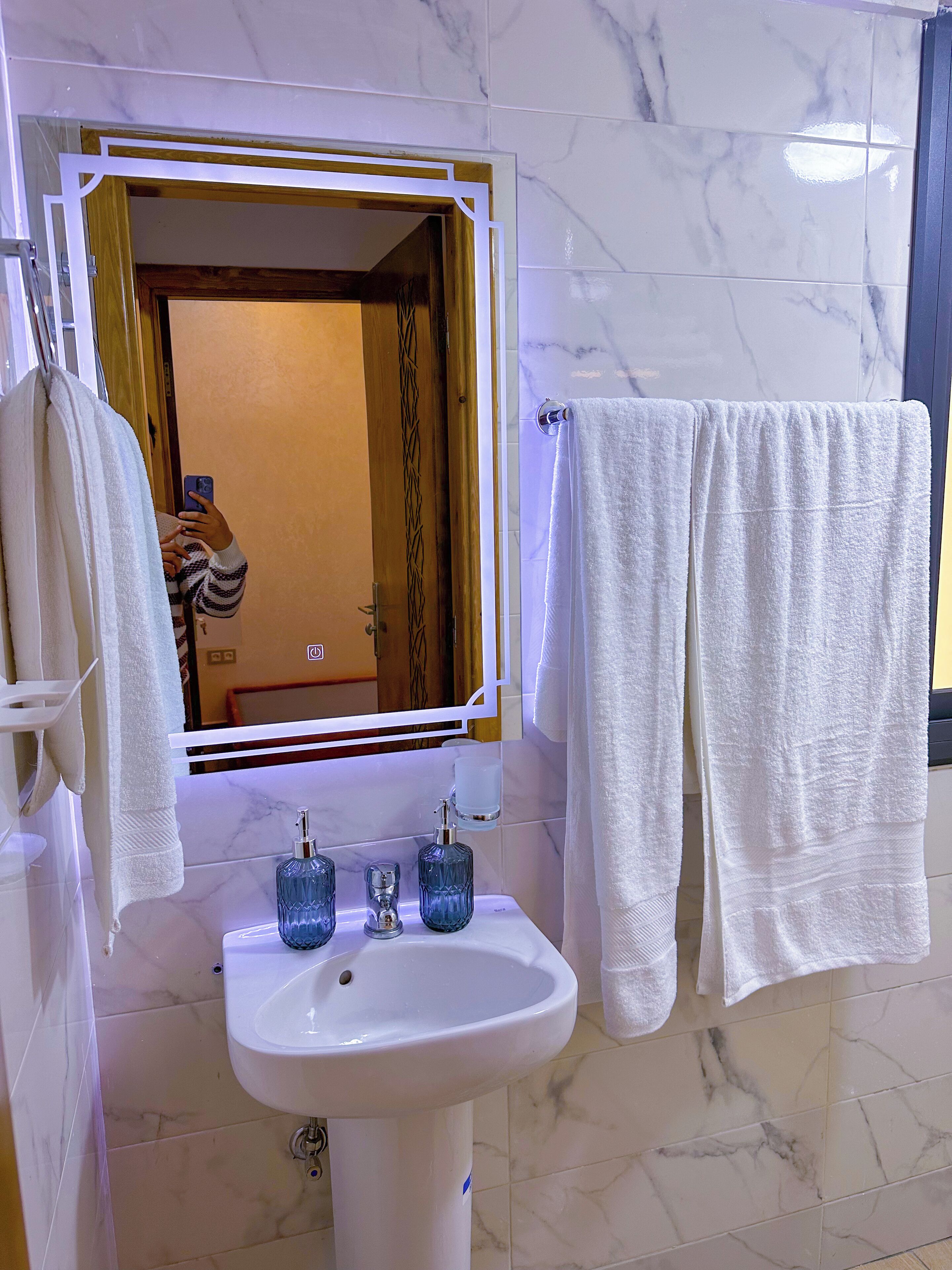 A bathroom with a white sink, a mirror with a gold frame, and two blue soap dispensers.