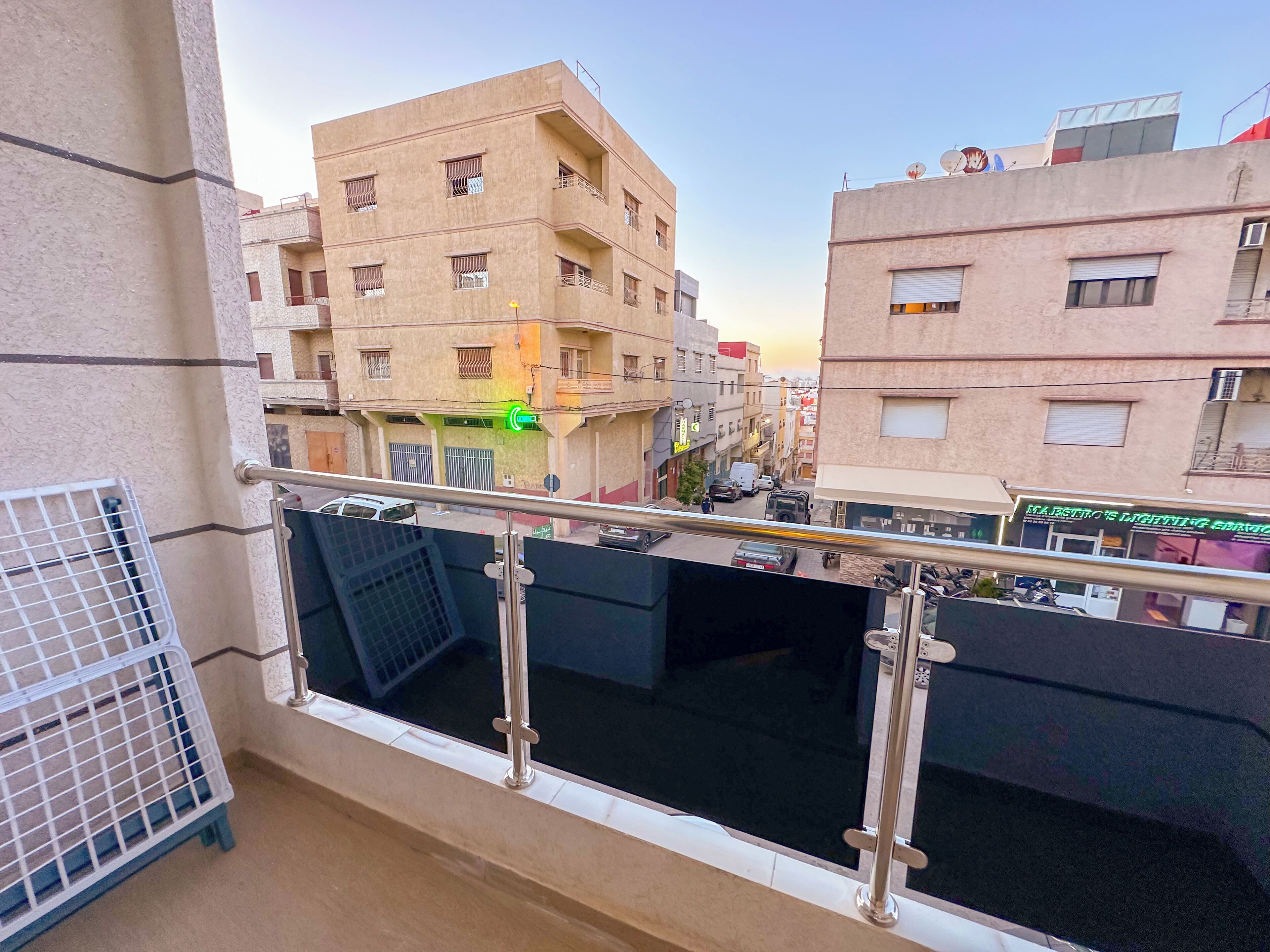 A balcony with a metal railing, a view of adjacent buildings, and a sign for 'MAJESTRO'S LIGHTING SERVICES'.