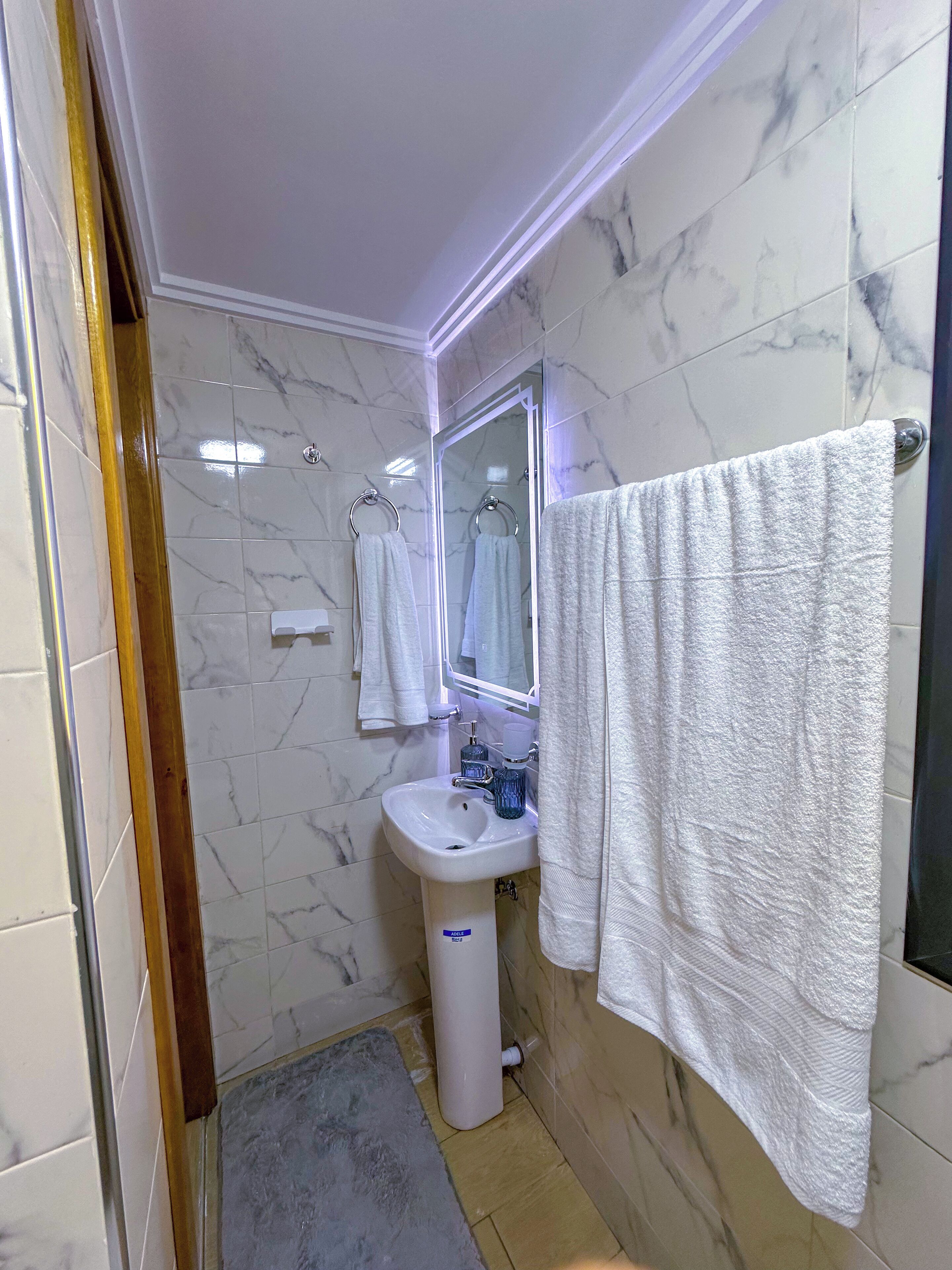 A bathroom with a marble-tiled wall, a white sink, a mirror, and a towel hanging on the wall.