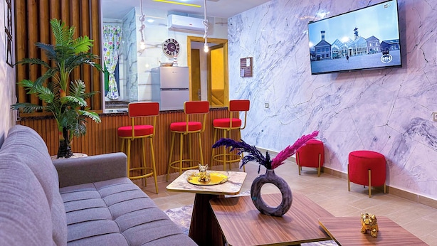Uma sala de estar moderna com um sofá, cadeiras vermelhas, uma televisão e um vaso decorativo.