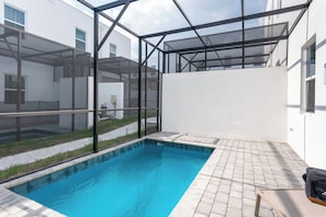 A swimming pool with a glass enclosure, surrounded by a paved patio and a white building. - Whimsy by Avantstay Pool 30min to Disney (Davenport)