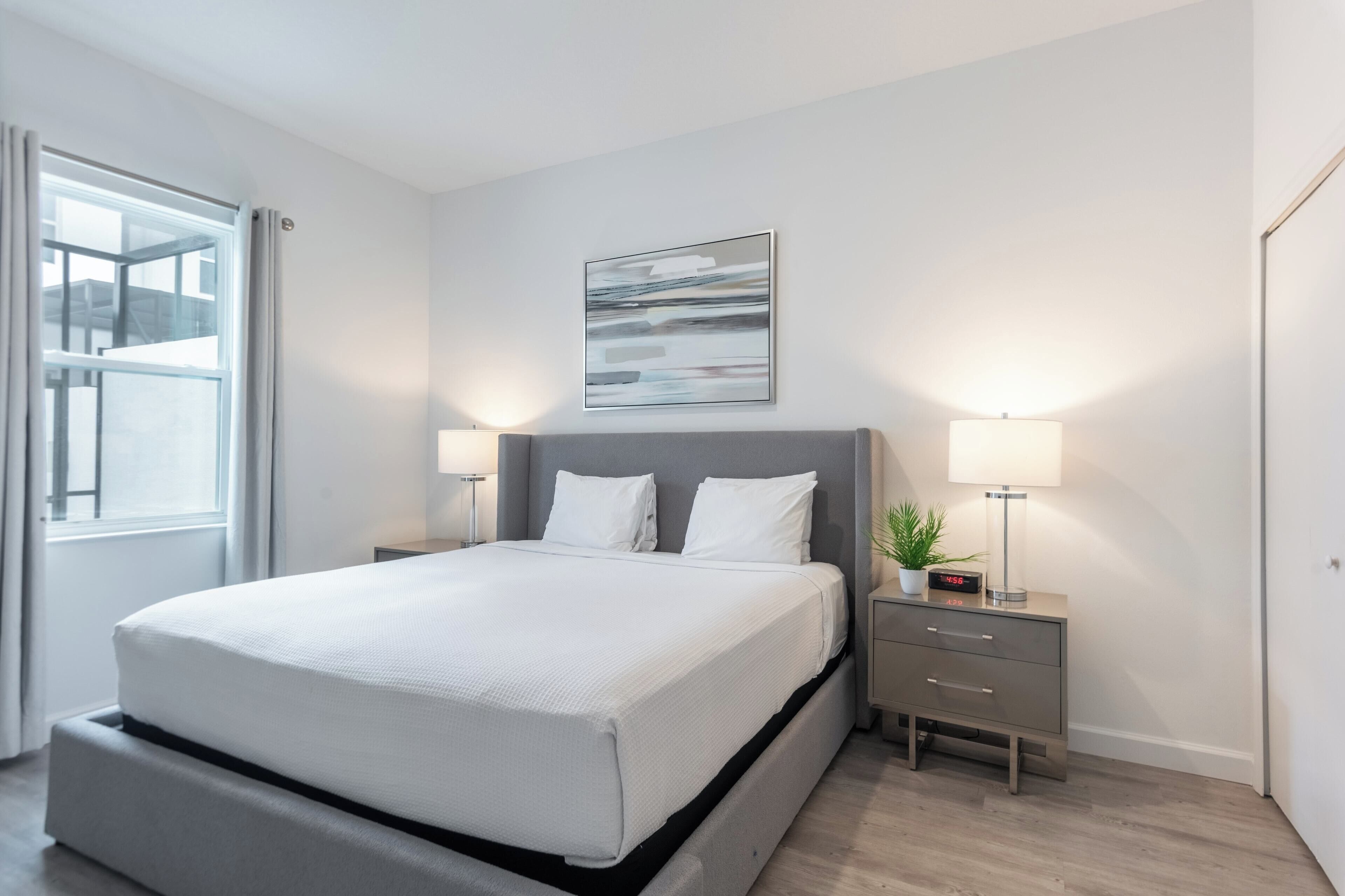 A modern bedroom with a large bed, bedside tables, a nightstand, and a window.