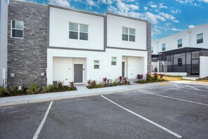 A modern two-story building with a garage door, a covered outdoor area, and a parking lot. - Whimsy by Avantstay Pool 30min to Disney (Davenport)