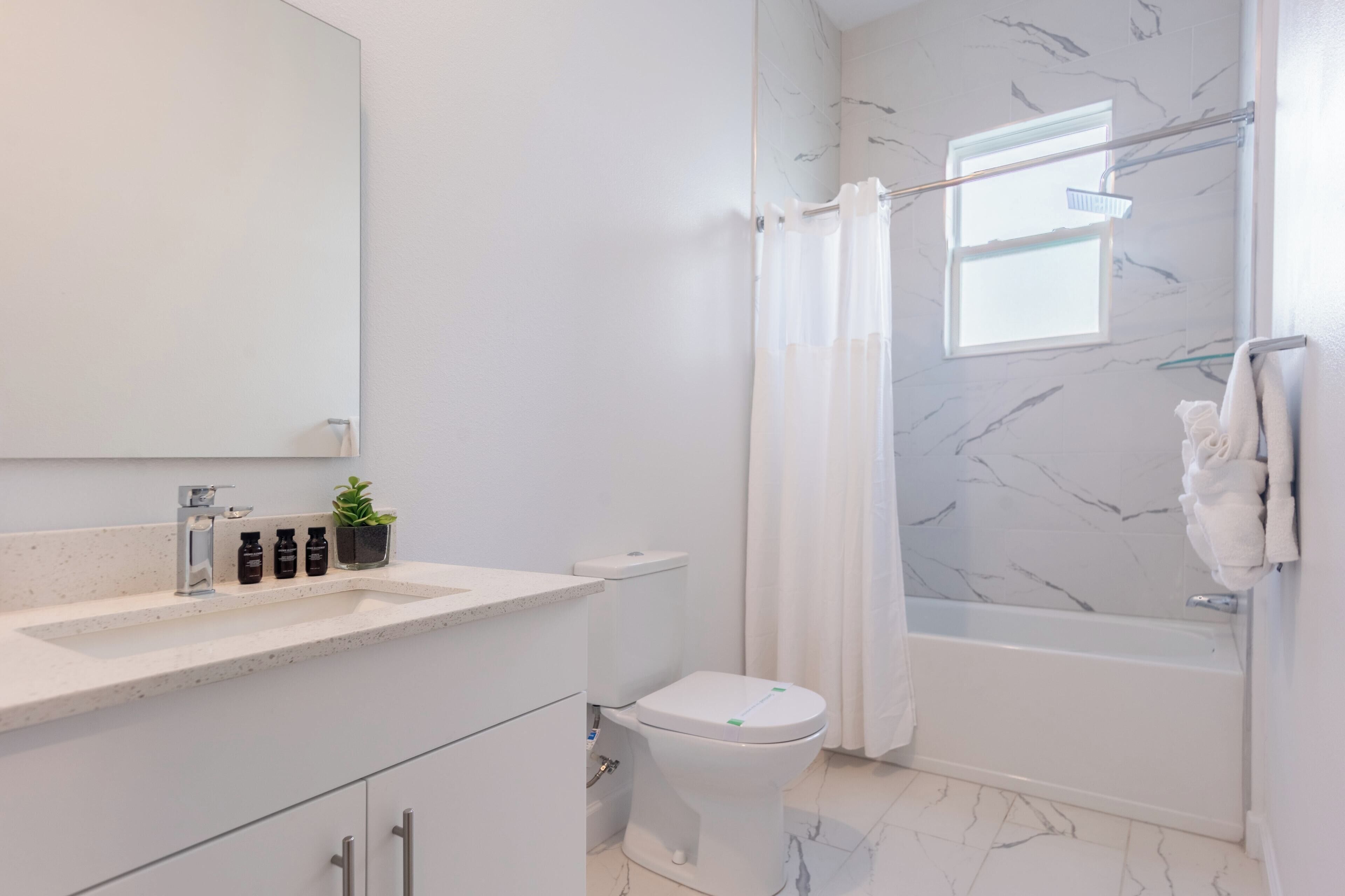 Een moderne badkamer met een marmeren vloer, een wit toilet, een badkuip en een douche met gordijn.