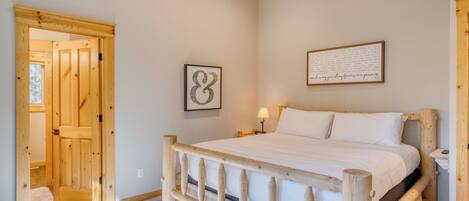 A bedroom with a wooden bed frame, a single bed, a nightstand with a lamp, a framed inspirational quote, and a door with a wooden frame.
