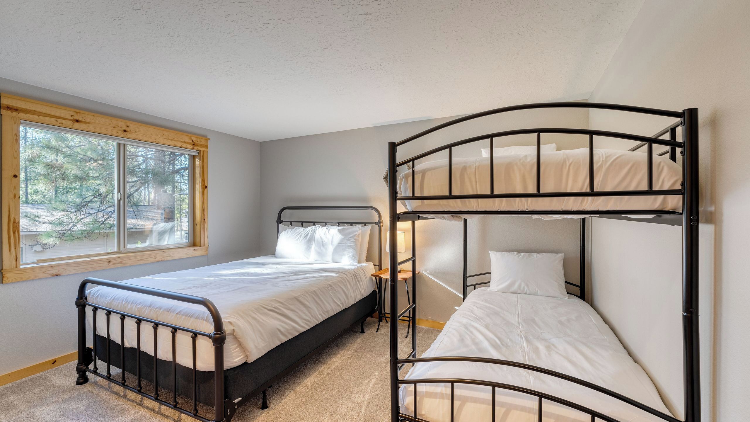A room with a single bed, a bunk bed, a window with a view of trees, and a carpeted floor.
