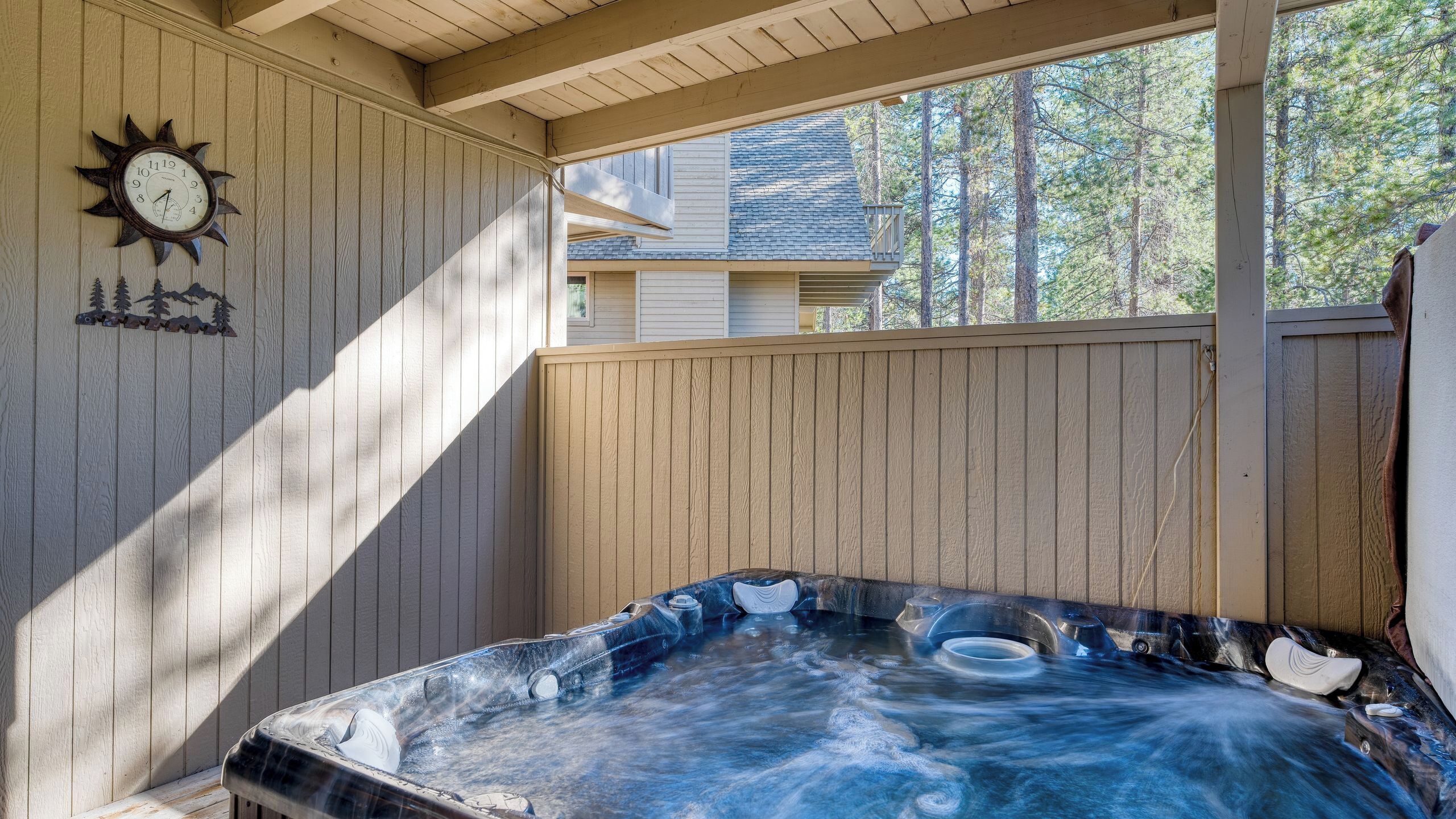 A hot tub in a covered outdoor area with a wooden deck and a clock on the wall.