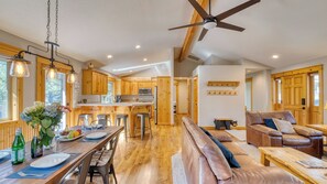 A spacious kitchen with wooden cabinets, a dining area with a table set for two, a leather sofa, and a ceiling fan. - Quail by Avantstay Great Location + Game Room, Hot Tub, & Deck! (Bend)