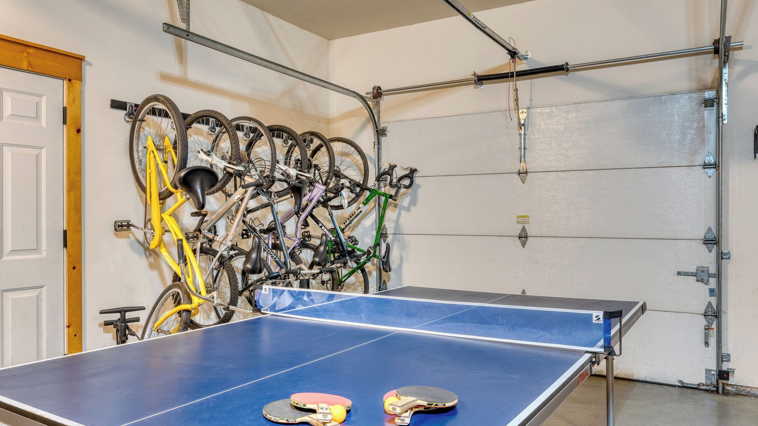 A ping pong table in a garage with bicycles mounted on the wall.