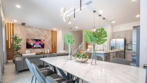 A modern kitchen with stainless steel appliances, a marble island, and a dining area with grey upholstered chairs.