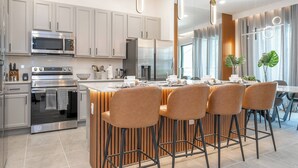 A modern kitchen with stainless steel appliances, a central island with bar stools, and pendant lighting.