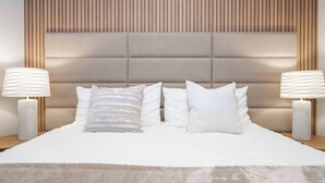 A modern bedroom with a tufted headboard, a large bed with white linens, two bedside lamps, and a neutral-toned rug.
