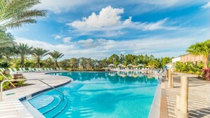 A swimming pool with a clear blue water, surrounded by lounge chairs and palm trees.