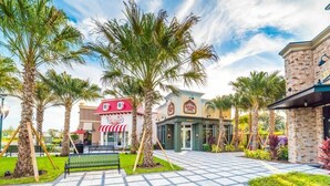 A plaza with palm trees, a playground, and buildings with signs for a restaurant and a shop.