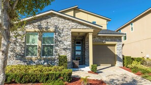 A modern two-story house with stone exterior walls, a front garage, and a well-maintained garden.