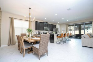A modern kitchen with dark cabinets, a dining area with a wooden table and chairs, and a living area with a sofa and chairs.