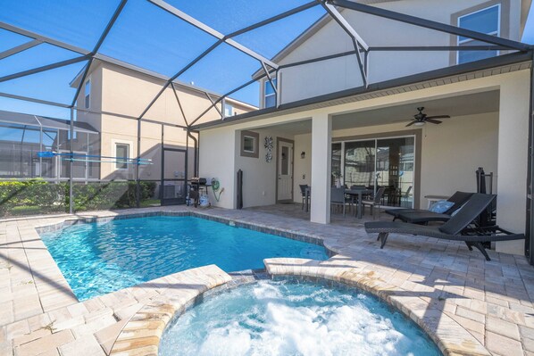 A swimming pool with a hot tub, surrounded by a covered patio area with lounge chairs and a ceiling fan.