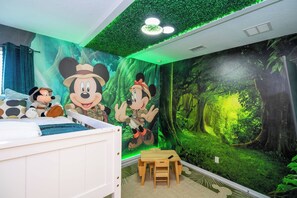 A child's bedroom with a forest-themed mural, a bed, a small table, and a chair.