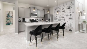 A modern kitchen with a central island, bar stools, and a wall with coffee-themed decorations. - DLuxx Resort Villa w/ Pool & Lazy River 8965 (Kissimmee)