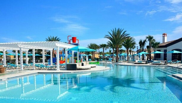 A clear blue pool with lounge chairs and umbrellas, surrounded by palm trees and a white gazebo structure. - DLuxx Resort Villa w/ Pool & Lazy River 8965 (Kissimmee)