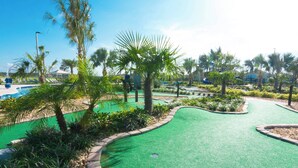 A golf course with a green artificial turf, palm trees, and a pool area.