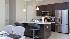 A modern kitchen with dark cabinets, stainless steel appliances, and a central island with bar stools. - Cozy Vacay 8 Miles From Disney Animal Kingdom 168 (Davenport)