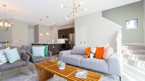 A modern living room with a grey sofa, two armchairs, a wooden coffee table, and a kitchen in the background. - Cozy Vacay 8 Miles From Disney Animal Kingdom 168 (Davenport)