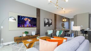 A modern living room with a large flat-screen TV, comfortable seating, a wooden coffee table, and a dining area with a bar. - Cozy Vacay 8 Miles From Disney Animal Kingdom 168 (Davenport)