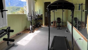 Een sportschool met een loopband, trainingsfietsen en een spiegelwand.