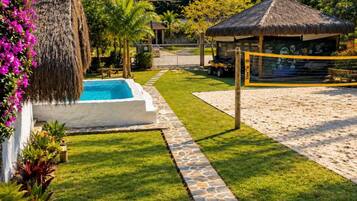 A pool area with a stone pathway, a thatched-roof structure, and lush greenery.