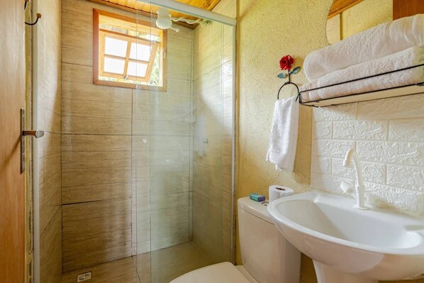 Un baño con ducha envuelta en cristal, un lavamanos con grifo blanco y un perchero con una flor roja.