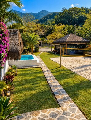 A pool area with a stone pathway, a thatched-roof structure, and lush greenery. - N5 - Chalé 2 Quartos Angra dos Reis (Angra dos Reis)