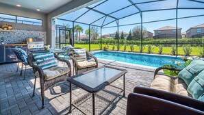 A covered outdoor area with a pool, wicker furniture, and a grill.