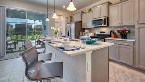 A modern kitchen with a large island, stainless steel appliances, and a view of a pool.