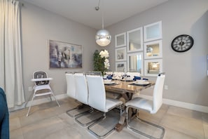 A dining area with a large table, white chairs, a high chair, a pendant light, and a clock on the wall. - DLuxx Vacay Disney 5 Suite House with Hot Tub 2633 (Kissimmee)