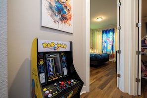 A Pac-Man arcade machine in a room with a bed and a colorful painting on the wall. - DLuxx Vacay Disney 5 Suite House with Hot Tub 2633 (Kissimmee)