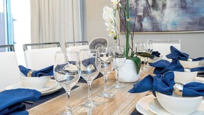 Una mesa de comedor dispuesta con platos blancos, copas de vino transparentes y servilletas azules.