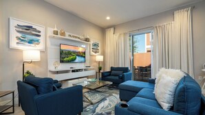 Una sala moderna con una televisión de pantalla plana, sofás azules, una mesa de centro de vidrio y un tapete decorativo.