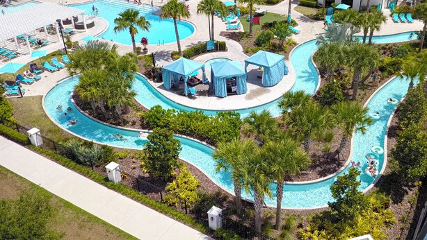 Un complexe hôtelier doté d’une grande piscine centrale, de plusieurs piscines plus petites et d’espaces ombragés avec des parasols.