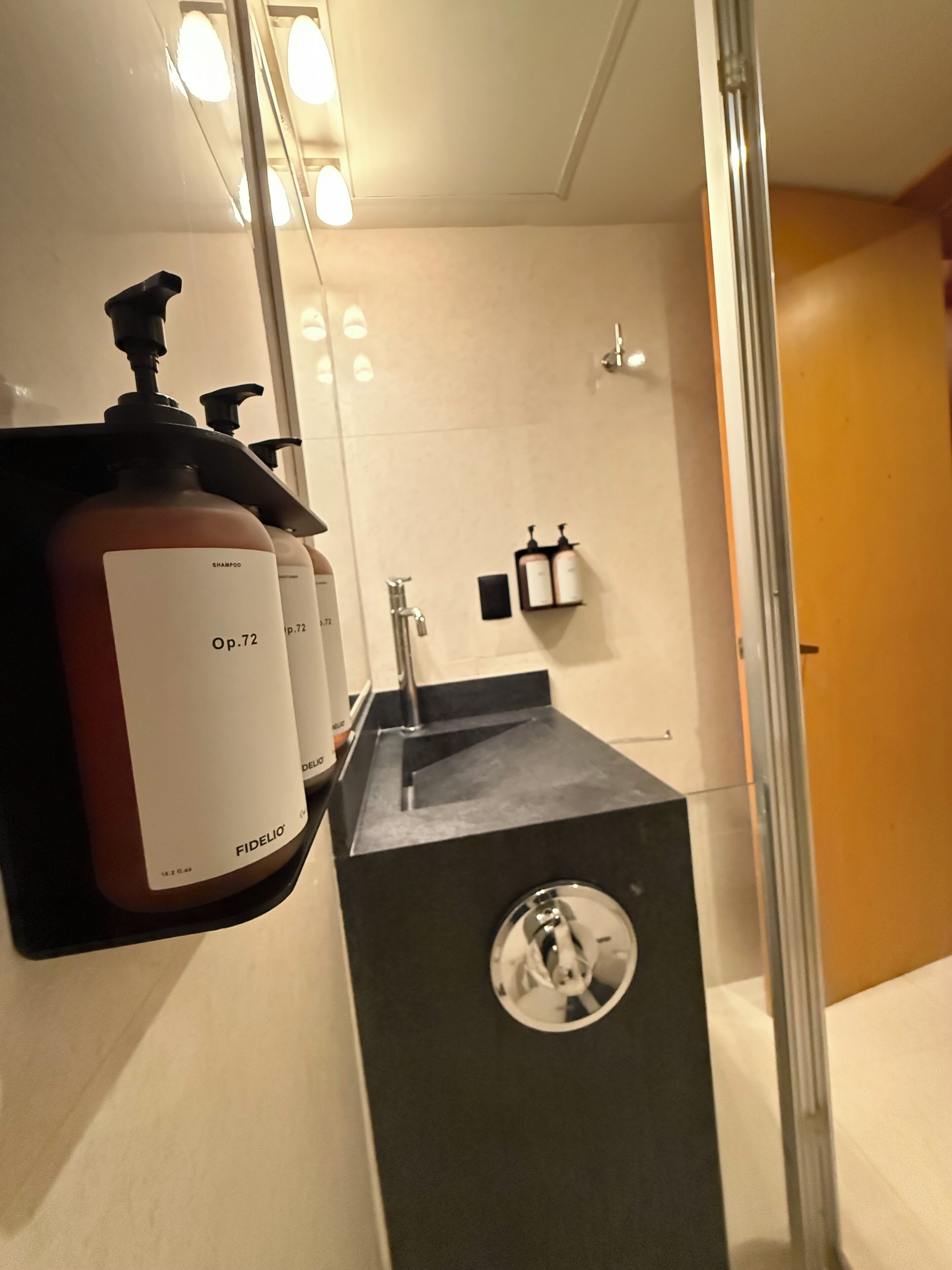 A modern bathroom with a black sink, a mirror, and two bottles of shampoo labeled 'Op.72'.