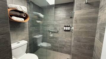 A modern bathroom with a glass-enclosed shower, a toilet, and a shelf with towels.