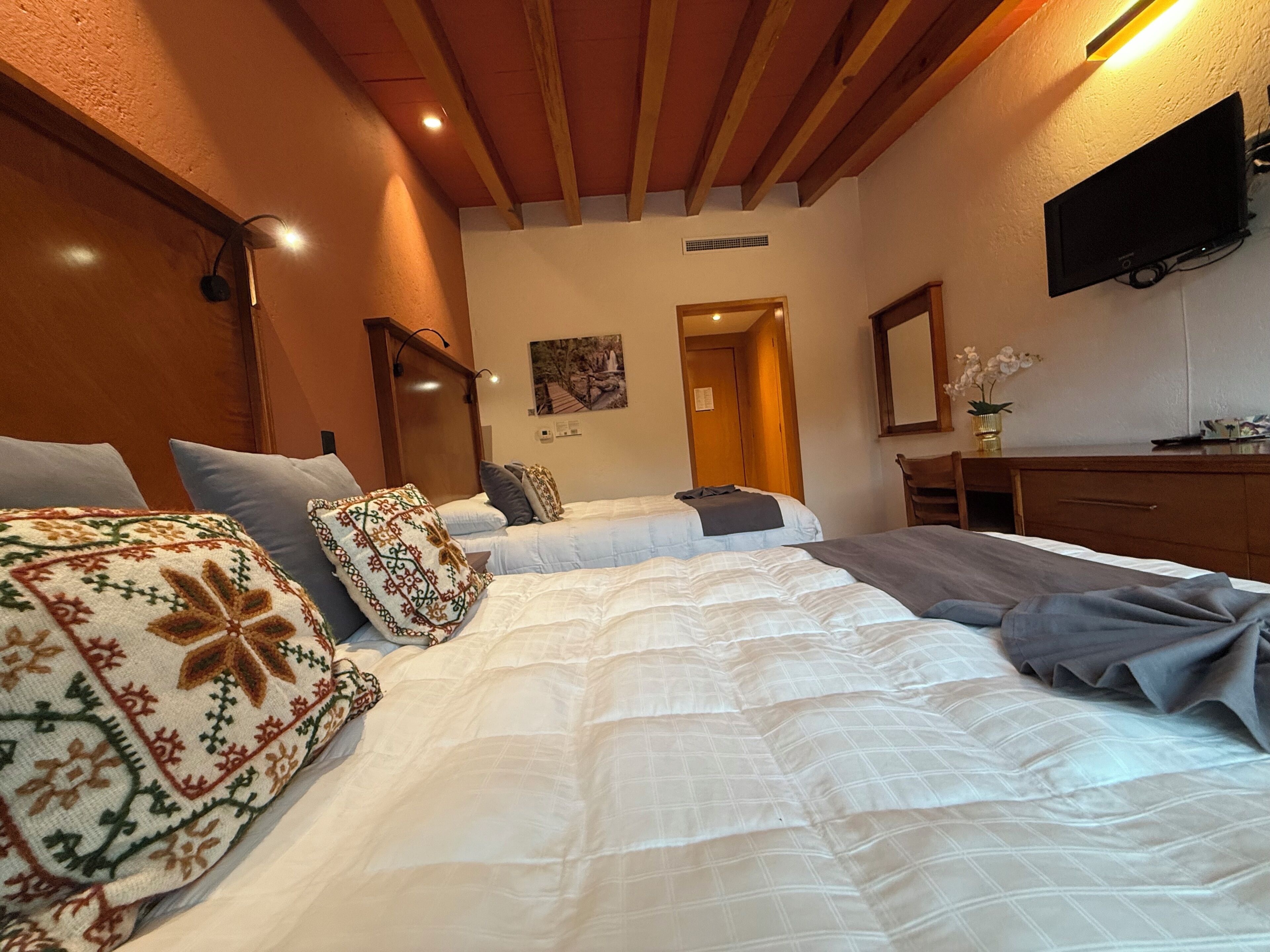 A bedroom with a large bed, two bedside tables, a dresser, a flat-screen TV, and a painting on the wall.