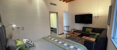 A modern hotel room with a bed, a sofa, a TV, and a small table.