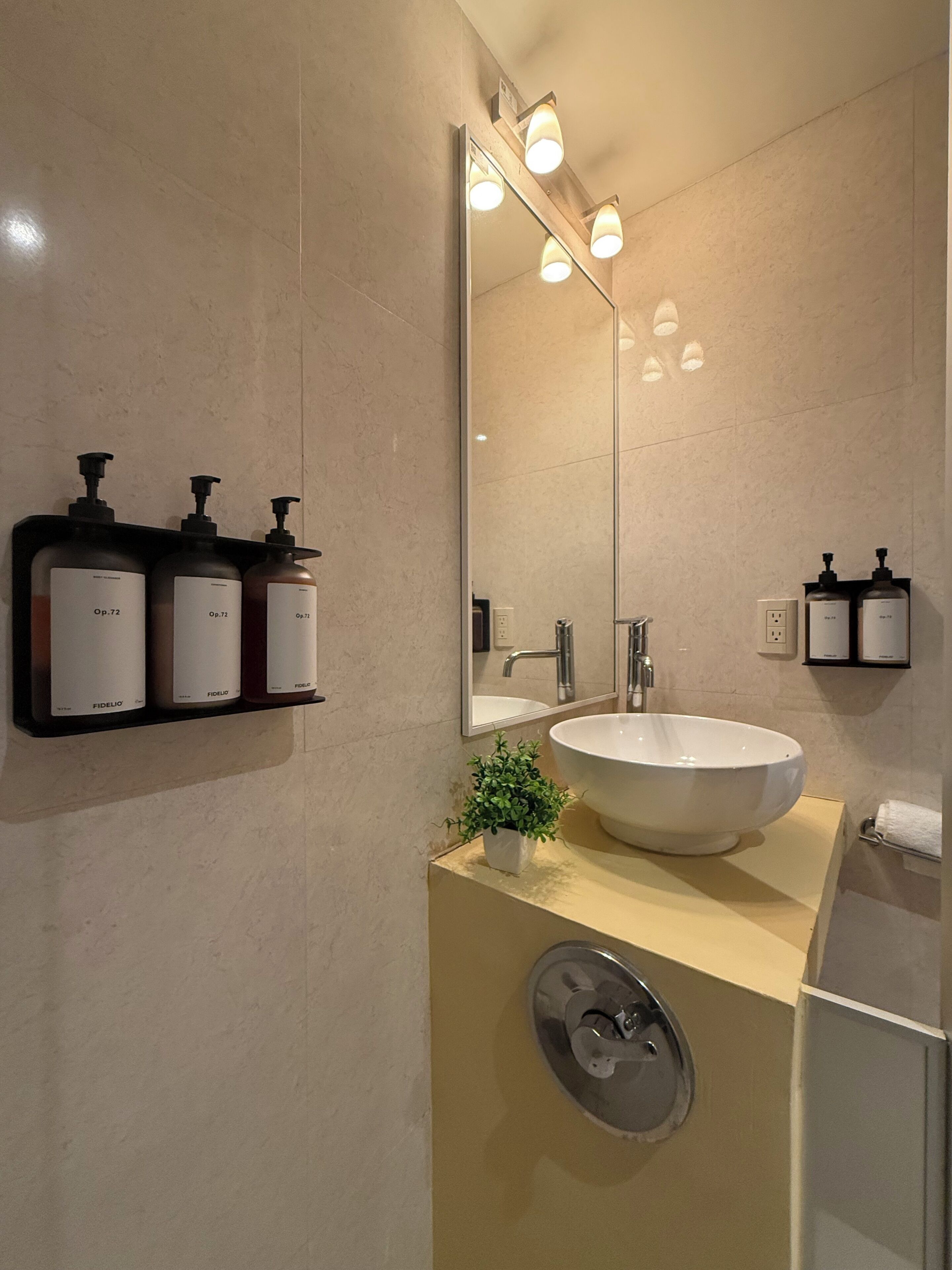A modern bathroom with a large mirror, a sink, and three bottles of shampoo on a shelf.